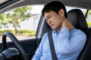 40代男性が車を運転中に寝違えによる首の痛みで困っている様子。振り向けず首を押さえているイメージ。