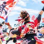 青空の下、色鮮やかな衣装を着た踊り手たちが鳴子を持って躍動するよさこいイベントの様子