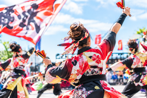 青空の下、色鮮やかな衣装を着た踊り手たちが鳴子を持って躍動するよさこいイベントの様子
